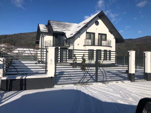 une maison blanche avec une clôture dans la neige dans l'établissement Vila Lorena, à Stejaru