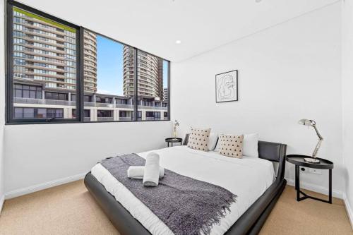 a white bedroom with a bed and large windows at Four bedroom apartment with facilities in Olympic Park in Sydney