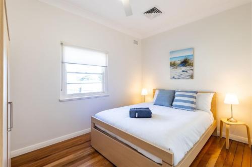 Un dormitorio blanco con una cama con una maleta. en Tomaree Cottage 12 Tomaree Road - 200 mtrs to Beach - Pet Friendly, linen, WiFi & aircon, en Shoal Bay