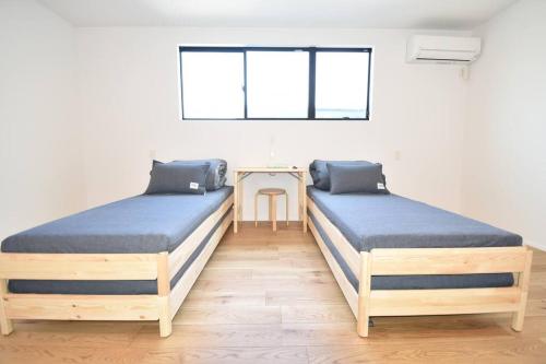 duas camas num quarto com uma mesa e uma janela em Enzo Ikeda A em Omura
