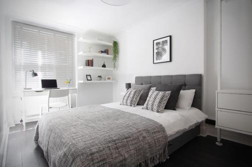 Luxury 2BR Flat in Hip Notting Hill في لندن: غرفة نوم بيضاء مع سرير مع وسائد ومكتب