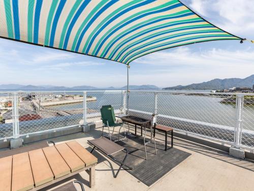 uma varanda com uma mesa, uma cadeira e um guarda-chuva em Omotenashi Hostel Miyajima em Hatsukaichi