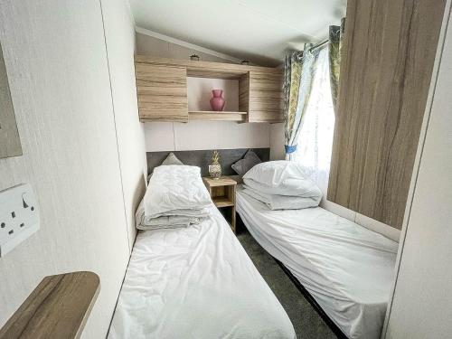 Duas camas num pequeno quarto com uma janela em Beautiful Caravan With Decking And Free Wifi At Highfield Grange Ref 26740wr em Clacton-on-Sea