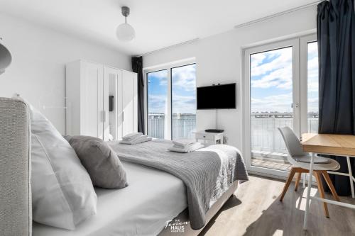 a white bedroom with a bed and a desk and windows at Seestern in Olpenitz