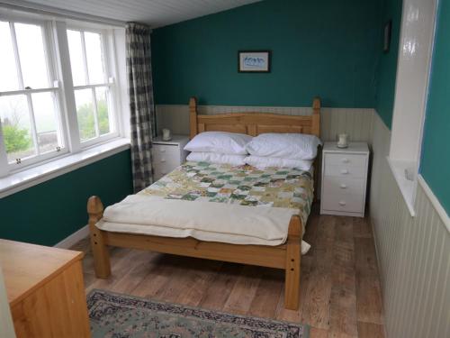 a bedroom with a bed with green walls and windows at The Drovers Cabin in Kirkcudbright