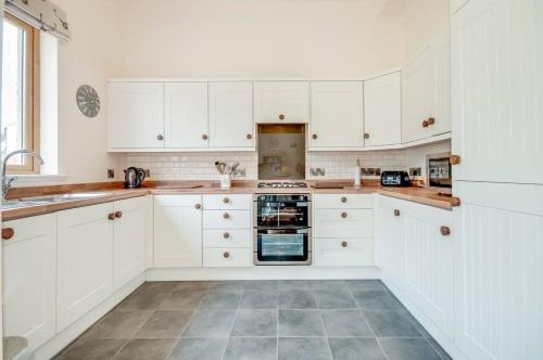 uma cozinha com armários brancos e piso em azulejo em Kinnen Cottage em Creetown