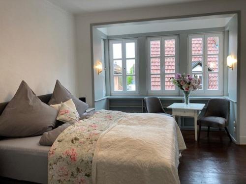 a bedroom with a bed and a table and two windows at Ferienwohnung Grete in Münsingen