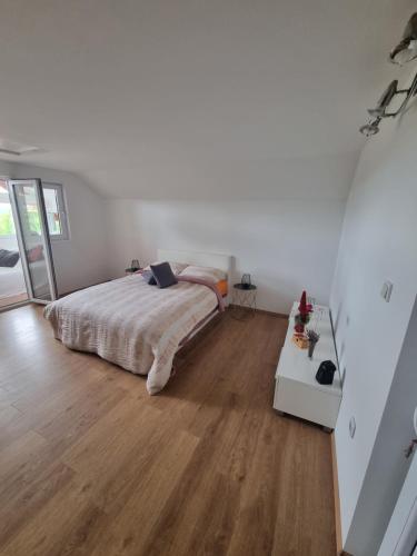 een witte slaapkamer met een bed en een houten vloer bij Kuća za odmor Mia in Bedekovčina