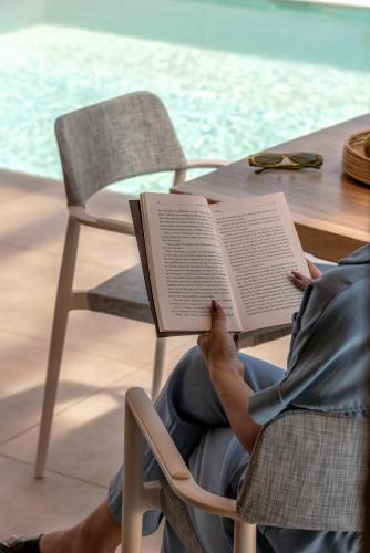 a person sitting in a chair reading a book at Pileas Villa, a Supreme Retreat by the Βeach, By ThinkVilla in Pigianos Kampos