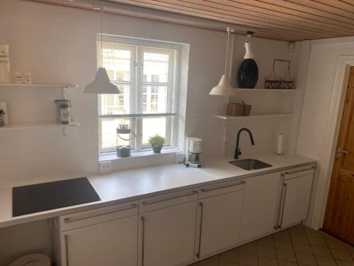 cocina con armarios blancos, fregadero y ventana en Knasborg Ferieboliger, en Ålbæk