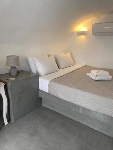 a bed with white pillows and a lamp on a table at AQUA SERENITY LUXURY SUITES SANTORINI in Foinikiá