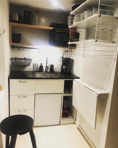 una pequeña cocina con armarios blancos y un taburete negro en Lilla huset med tennisbana, 