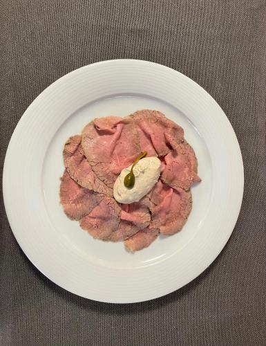 a white plate with a piece of meat with a pickle on it at Hotel Il Grappolo D'Oro in Monforte dʼAlba