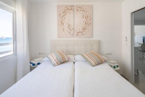a white bedroom with a bed with two pillows at El Acuario - Primera línea y todas las ventanas dan al mar in Cullera