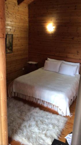 Cama en habitación de madera con edredón blanco en Gioia Resort, en Voskopojë