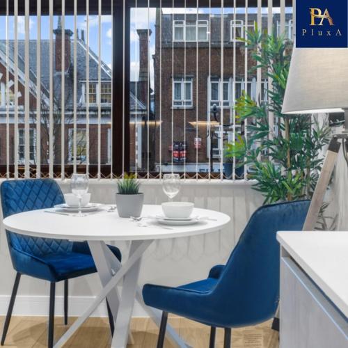a white table and blue chairs in a room with a window at Pluxa Larimar - Spacious Apt with Private Entrance, Workspace & Wi-Fi in Harrow