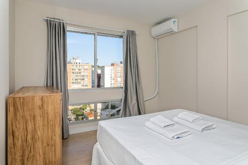 Un dormitorio con una cama blanca y una ventana. en 500m do Top Market | Vista Parcial do MAR #CA36, en Florianópolis