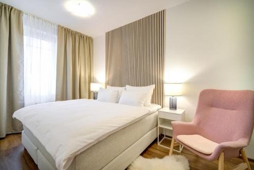 een slaapkamer met een wit bed en een roze stoel bij Urban Apartments in Brno