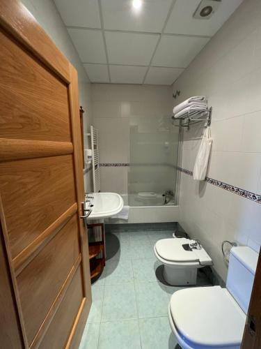 een badkamer met 2 toiletten, een wastafel en een deur bij Hostal Villa el Colmenar in Mombeltrán