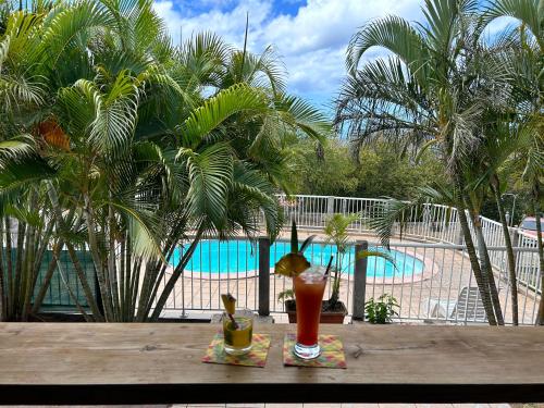 a drink on a table next to a pool at Gîtes Hotel Couleur Caraibes in Bouillante