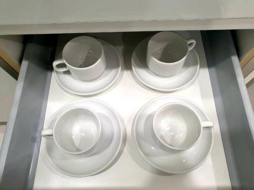 four white cups and saucers on a shelf at Charming Studio 1BR 1LR Condo Georgetown 魅力一室一厅套房 in George Town