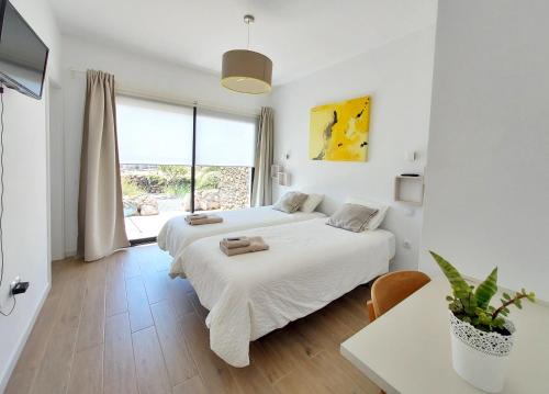 Habitación blanca con 2 camas, mesa y escritorio. en Villa en Lajares. Fuerteventura, en Lajares