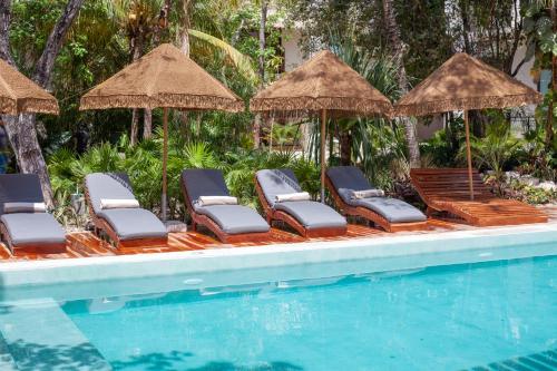 um grupo de cadeiras e guarda-sóis ao lado de uma piscina em Prana Boutique Hotel Tulum em Tulum