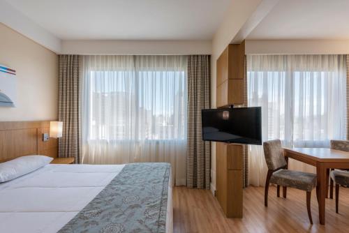 a hotel room with a bed and a desk and a television at Monreale Plus São José dos Campos in São José dos Campos