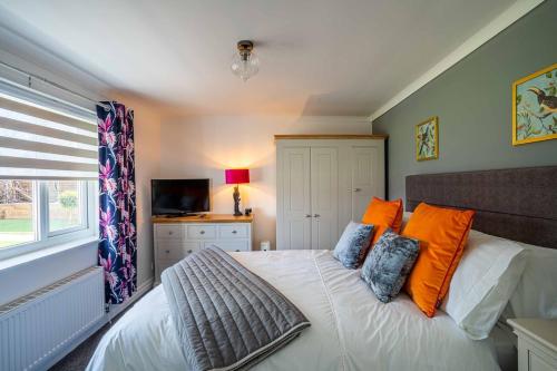 a bedroom with a bed with orange pillows and a television at 1 The Cottage in Upholland