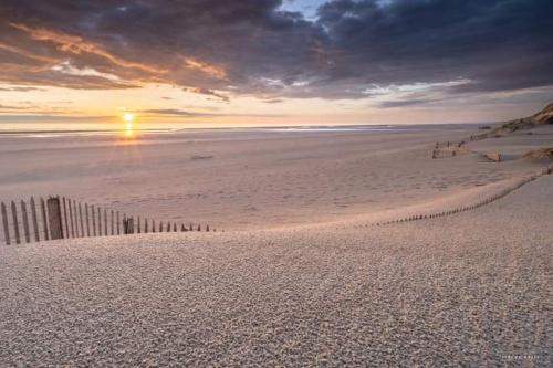 a sunset on a beach with a fence in the sand at L'escale du désir, Spa privatif in Calais