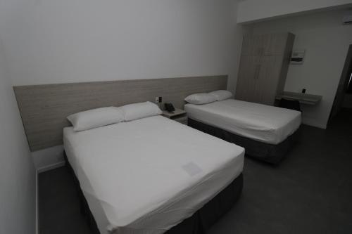 two beds in a small room with white sheets at Hotel Royal Brasil in Paramaribo