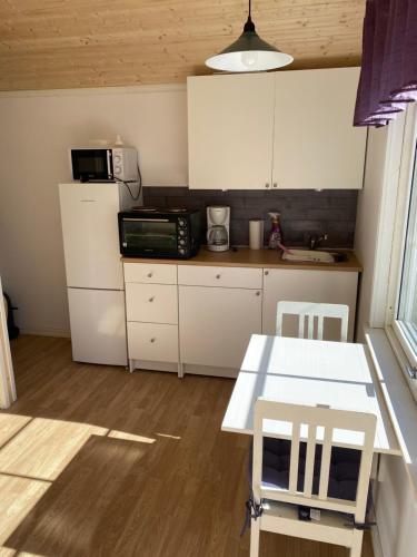 a kitchen with white cabinets and a white table and chairs at Söt liten stuga för 2 in Strömstad