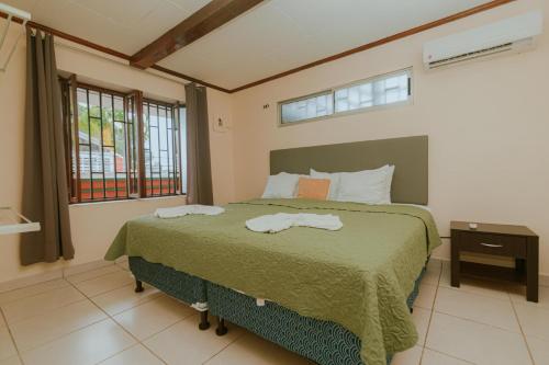 a bedroom with a bed with a green comforter and windows at Quepos Inn in Quepos