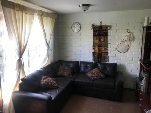ein schwarzes Ledersofa in einem Wohnzimmer mit einer Uhr in der Unterkunft Casa full amoblada: 3 dormitorios + estacionamiento in Coquimbo