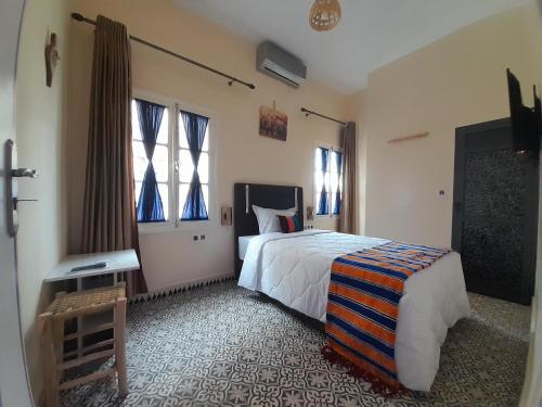 a bedroom with a bed and a table and windows at Hotel Mentaga in Taroudant