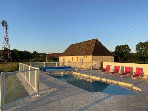 une piscine avec des chaises rouges et un bâtiment dans l'établissement Gite de Born avec piscine privée au coeur de la campagne, à Born-de-Champs