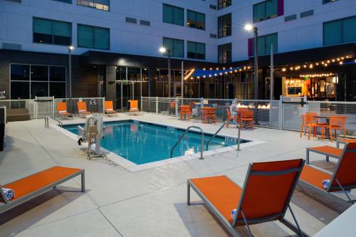 a swimming pool with chairs and tables and a building at Aloft Charlotte Airport in Charlotte