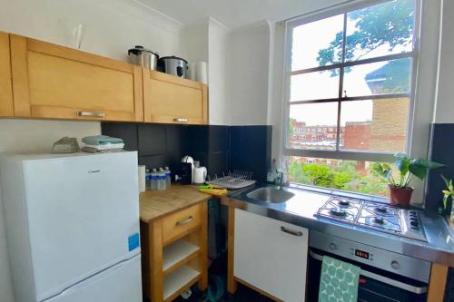 La cuisine est équipée d'un réfrigérateur blanc et d'un évier. dans l'établissement 2 Bedroom Flat in Camberwell Green - Central Location with excellent connections to tourist attractions and main London airports, à Londres