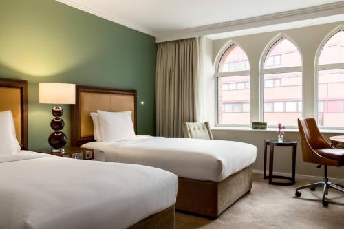 a hotel room with two beds and a desk and two windows at St. Pancras Renaissance Hotel London in London