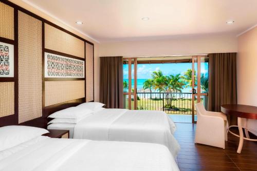 Habitación de hotel con 2 camas, mesa y balcón. en Sheraton Samoa Beach Resort, en Mulifanua