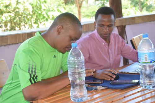 two men sitting at a table with a bottle of water at Kili View Lodge in Moshi