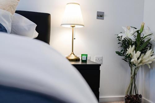 une lampe sur une table à côté d'un lit fleuri dans l'établissement Khayat Homes - The Cosmo - Two Bed, à Londres