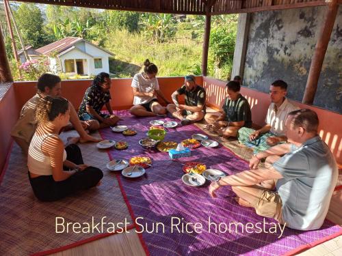 un grupo de personas sentadas alrededor de una mesa comiendo comida en Sun Rice Homestay, en Ruteng