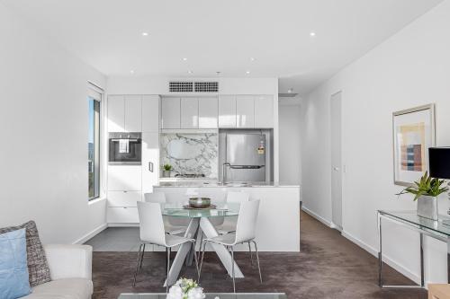 a white kitchen with a table and chairs at Swainson on Hindmarsh in Adelaide
