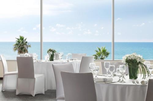 a restaurant with white tables and chairs and the ocean at Sheraton Grand Tel Aviv in Tel Aviv
