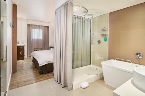 a bathroom with a tub and a shower and a bed at Protea Hotel by Marriott O R Tambo Airport in Kempton Park