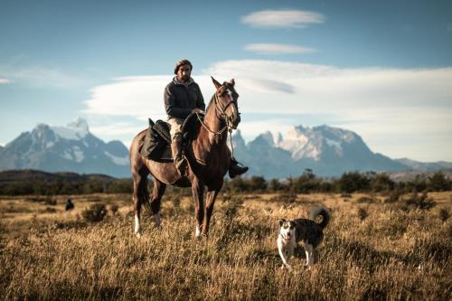 un hombre montando un caballo en un campo con un perro en Pampa Lodge, Quincho & Caballos, en Torres del Paine