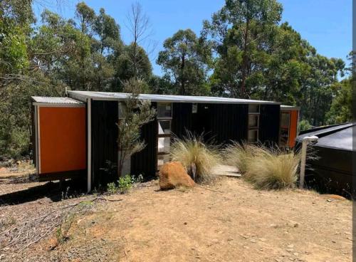 a black and orange house in a field with trees at Francis Lane Tiny Studio in Adventure Bay