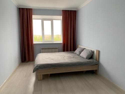 a bedroom with a bed and a window with red curtains at Апартаменты в районе Болашак in Aktobe