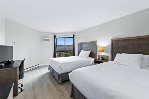 a hotel room with two beds and a desk and a television at The Vista Inn in Kamloops